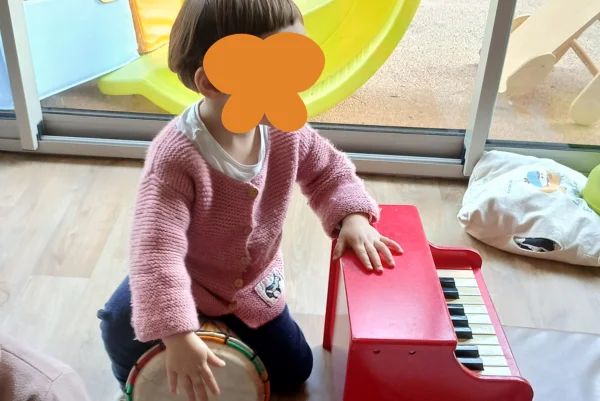 Crèche Les Bébés Explorateurs petite fille qui joue d'un tambour et d'un piano rouge