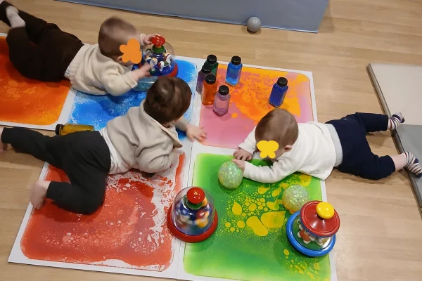 Crèche les Bébés Explorateurs trois bébés jouent au sol sur des tapis de couleurs