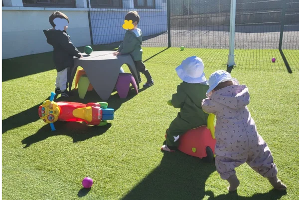 Quatres enfant jouent à l'intérieur, deux enfants autour d'une table et deux bébés sur un porteur