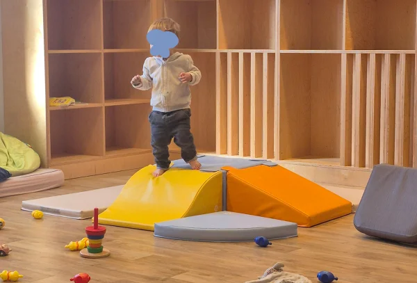 Dans une crèche Les Bébés Explorateurs, un enfant marche sur des modules de motricité de couleurs 